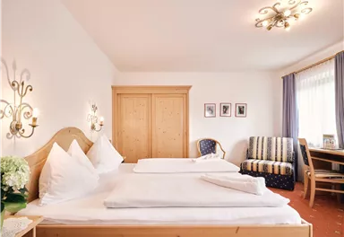 Ein gemütliches Zimmer mit zwei Betten und einem Fenster, das Tageslicht hereinlässt. Zarte Farben und Holzdetails sorgen für eine einladende Atmosphäre.