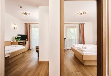 Ein helles, modernes Zimmer mit Holzfußboden und großen Fenstern. Das Zimmer ist einfach und gemütlich eingerichtet, mit einem Doppelbett und einem Einzelbett.