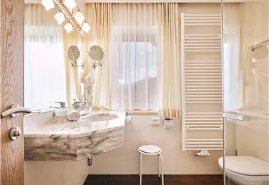 Ein modernes Badezimmer mit einer eleganten Waschbeckenanlage und viel natürlichem Licht. Die hellen Vorhänge und die stilvolle Beleuchtung schaffen eine einladende Atmosphäre.