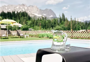 Ein schöner Pool mit Blick auf die Berge. Eine Karaffe mit Wasser und Zitronen steht auf einem Tisch.