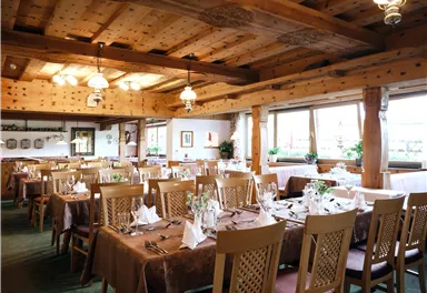 Ein gemütliches Restaurant mit Holzmöbeln und schön dekorierten Tischen. Große Fenster sorgen für viel Tageslicht.