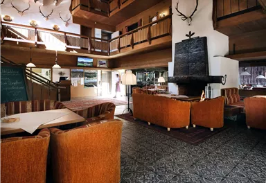 Eine gemütliche Lobby mit Holzelementen und bequemen orangefarbenen Sitzen. Im Hintergrund sind große Fenster und eine angenehme, einladende Atmosphäre zu sehen.