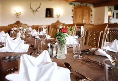 Ein elegant gedeckter Tisch in einem gemütlichen Restaurant. Die Tischdekoration besteht aus Servietten, Gläsern und einem Blumenstrauß.