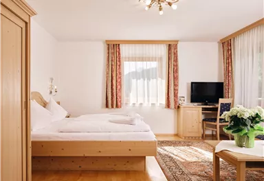 Ein gemütliches Schlafzimmer mit einem Doppelbett und Holzmöbeln. Große Fenster sorgen für viel Tageslicht und eine entspannte Atmosphäre.