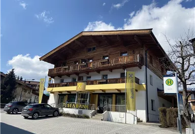 Ein modernes Bankgebäude im alpinen Stil mit Holzverkleidung. Parkplätze sind vor dem Gebäude sichtbar.