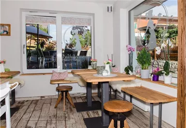 A cozy café with wooden chairs and tables. Plants and flowers decorate the windowsill and the atmosphere is inviting.