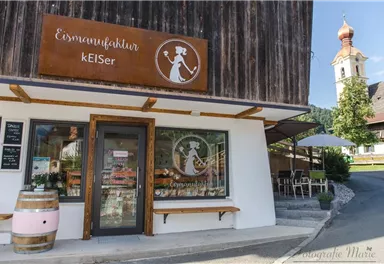 A charming ice cream parlor with an inviting facade and a large window. In the background, you can see a church tower and a beautiful landscape.