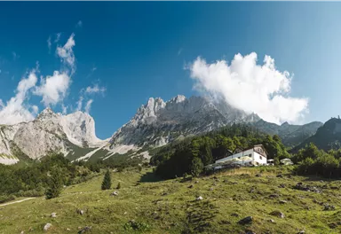 A picturesque mountain landscape with tall rocks and fresh greenery. In the foreground stands a simple building, surrounded by nature.
