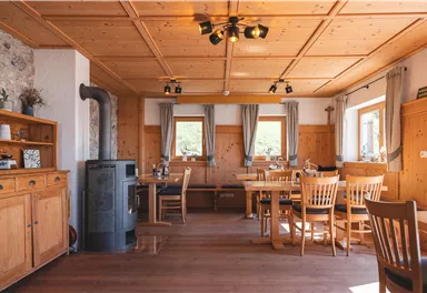 A cozy room with wooden furniture and a wood stove. Large windows let in a lot of light and create an inviting atmosphere.