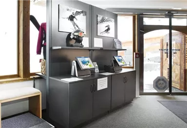 A modern reception area with a black piece of furniture and two screens. Sports photos hang on the walls, and large windows offer a view outside.