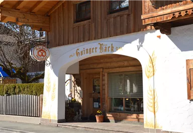 A traditional, cozy building with wooden cladding and an inviting entrance. Above the entrance, the name "Ginger Bäck" adorns the façade.