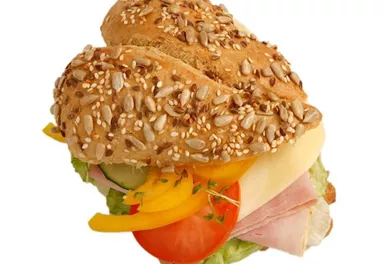 A whole grain sandwich roll with sesame, filled with ham, cheese, fresh vegetables, and lettuce. It looks appetizing and healthy.