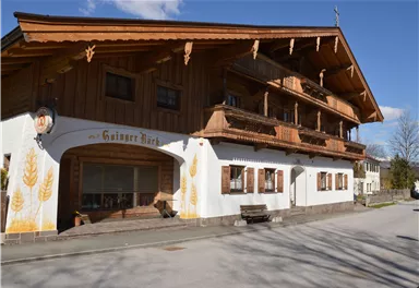 A traditional Bavarian guesthouse with a wooden-paneled facade. It has large balconies and appears to be situated in a quiet rural setting.