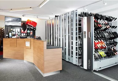 A modern sales room with a reception desk and shoe shelves. On the right side, there are various pairs of shoes in different colors.