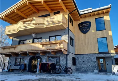 Ein modernes Gebäude im alpinen Stil mit Holz- und Steinfassade. Vor dem Haus stehen Kleidung zum Verkauf und ein Fahrrad.