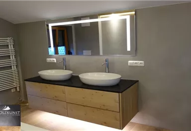 Ein modernes Badezimmer mit zwei Waschbecken und einem stilvollen Spiegel. Die Holzschränke und die schlichte Wandgestaltung schaffen eine elegante Atmosphäre.