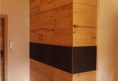 Ein moderner Holzschrank mit einer Kombination aus hellem Holz und einer schwarzen horizontalen Linie. Der Schrank ist in einem stilvollen Raum mit warmem Licht platziert.