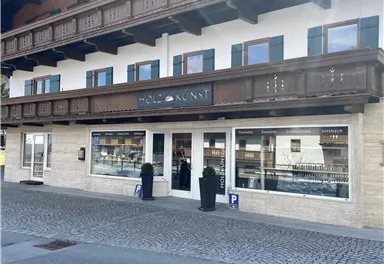 Ein modernes Gebäude mit einem Holzveranda und großen Fenstern. Der Schriftzug „HOLZ KUNST“ ist gut sichtbar über dem Eingang.