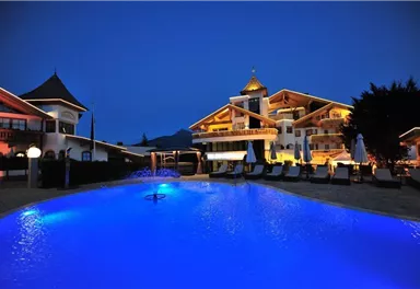 A beautiful hotel with a illuminated outdoor area and a blue pool. The atmosphere is calm and inviting in the evening.