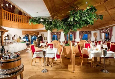A stylish restaurant with wooden elements and cozy tables. Red chairs and a large plant in the center create an inviting atmosphere.