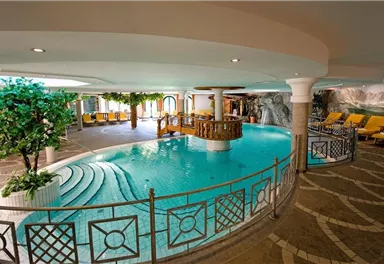 An elegant swimming pool with clear water and a central waterfall. Surrounded by cozy loungers and green plants, it offers a relaxing atmosphere.