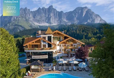A beautiful hotel with a pool and loungers, surrounded by picturesque mountains. The nature in the background creates a relaxed atmosphere.