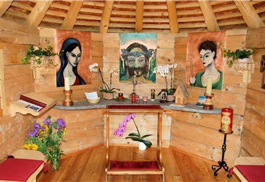 A cozy room with wood paneling and pictures on the wall. In the center is a table with flowers and candles.