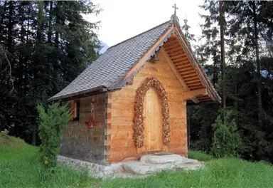 A small wooden church stands amidst trees. Surrounded by green grass, it appears peaceful and inviting.