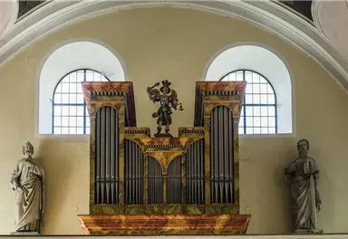 A magnificent church organ with golden embellishments and an angel statue in the center. On either side, there are figures that emphasize the sacred atmosphere.