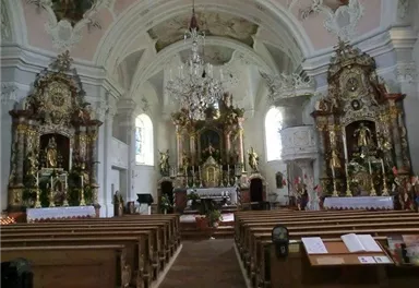 An elegant church with richly adorned altars and an impressive ceiling. The pews are neatly arranged, and the atmosphere is quiet and peaceful.