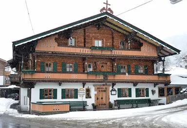 A traditional wooden house in Bavarian style, surrounded by snow. The green shutters and balconies give the building a charming look.