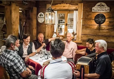 A sociable group of people in a rustic restaurant. They are chatting, singing, and playing traditional music.