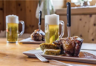 A delicious dish with meat and sides on a plate. In the background, there are two glasses of beer.