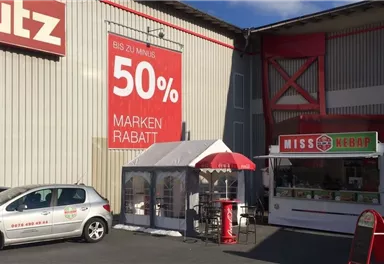 A busy parking lot in front of a store with a large sale sign for 50% brand bargains. Next to the building stands a food truck named "MISS KEBAB".