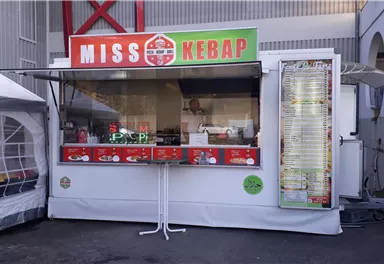A kebab stand named "Miss Kebap" with a large menu at the front. The stand is clean and well-lit, ideal for outdoor snacks.