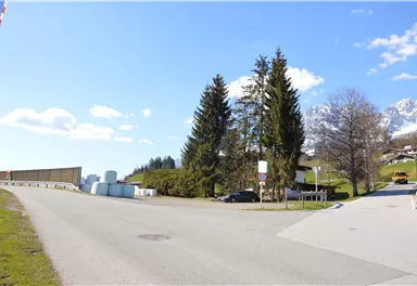 Eine ruhige ländliche Straße mit Bäumen und einem Blick auf die Berge. Auf der linken Seite stehen mehrere runde, weiße Objekte.