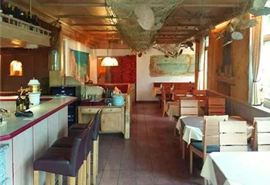 A cozy restaurant with wooden furniture and tablecloths. The decor features maritime elements and an inviting atmosphere.
