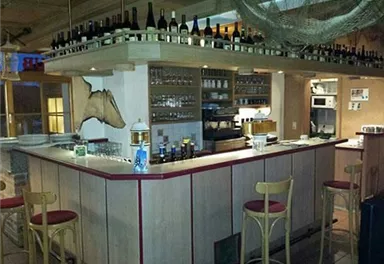 A cozy bar with wooden furniture and a counter decorated with wine bottles. A few bar stools are available to provide seating.
