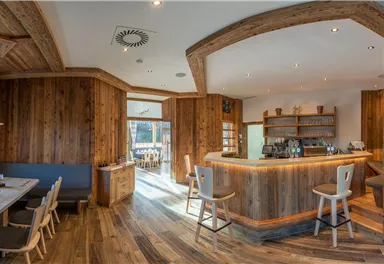 A modern restaurant with wooden elements and a cozy atmosphere. The bar is well stocked, and there is a view of the outdoors.