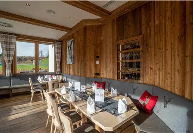 A cozy restaurant with wooden walls and a large window. The tables are festively set and there are comfortable seating options.