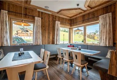 A cozy dining room with wooden walls and large windows. There are tables with wooden chairs and an inviting atmosphere.