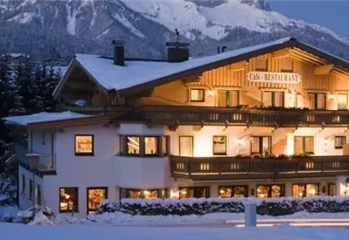 A cozy hotel in the snow with illuminated windows. In the background, snow-covered mountains and trees can be seen.