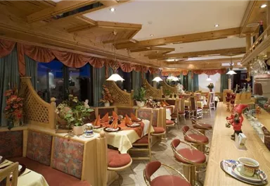 A cozy restaurant with wooden furniture and soft lights. The tables are beautifully set and decorated with plants.
