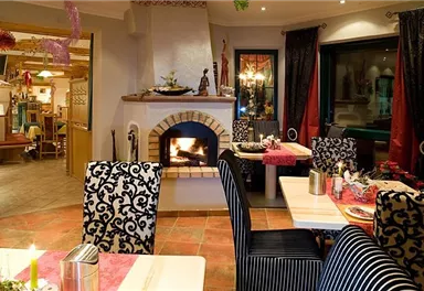 An inviting restaurant with a cozy atmosphere and an open fireplace. The tables are elegantly set and there are festive decorations.