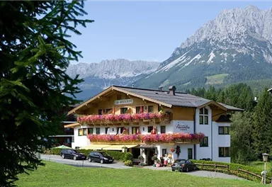 A charming chalet in the mountains with colorful flowers on the balconies. In the background, majestic mountains stretch under a blue sky.