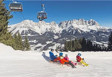 A group of skiers is sitting on a snow-covered slope. In the background, majestic mountains and a blue sky can be seen.