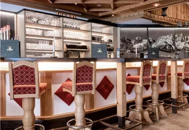 A modern bar with high wooden stools and an elegant counter. The room has a cozy atmosphere with warm lighting and a rustic decor.