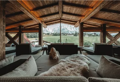 A cozy room with wooden beams and large windows offering a view of the mountains. The decor is modern and inviting.