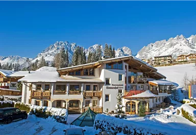 A cozy hotel in a snow-covered landscape. In the background, majestic mountains and a clear blue sky can be seen.