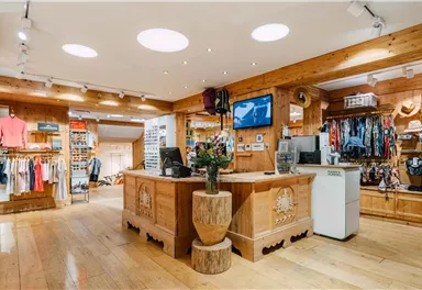 A cozy shop with wooden decor and a variety of clothing items. At the checkout, there is a plant in a decorative pot.